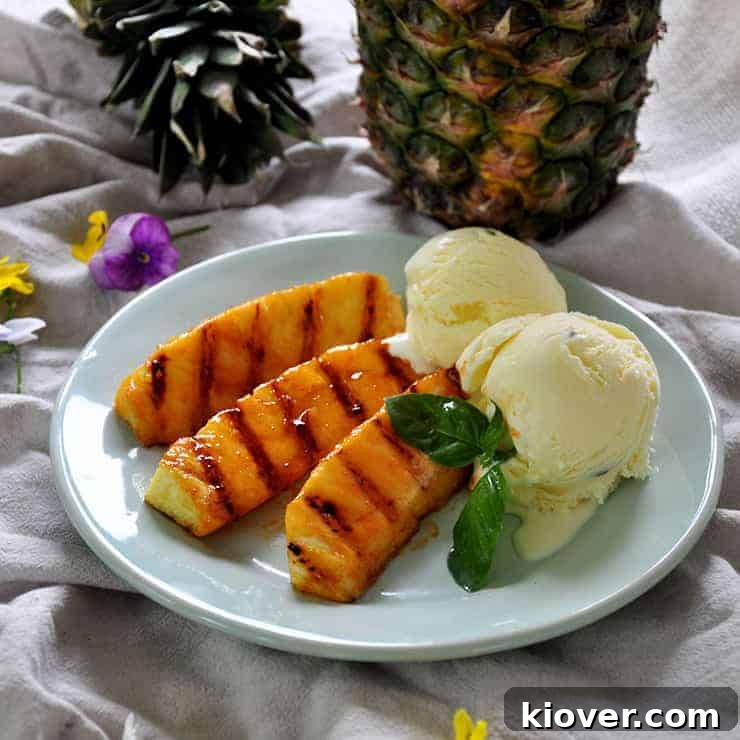 Grilled pineapple with a side of basil ice cream on a plate with pineapple in the background and some decorative flowers.
