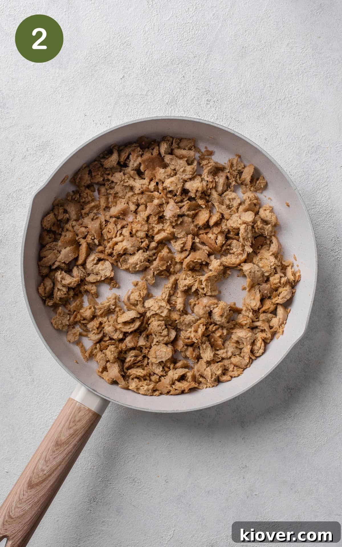 Crumbled sausages browning in a large skillet with olive oil.