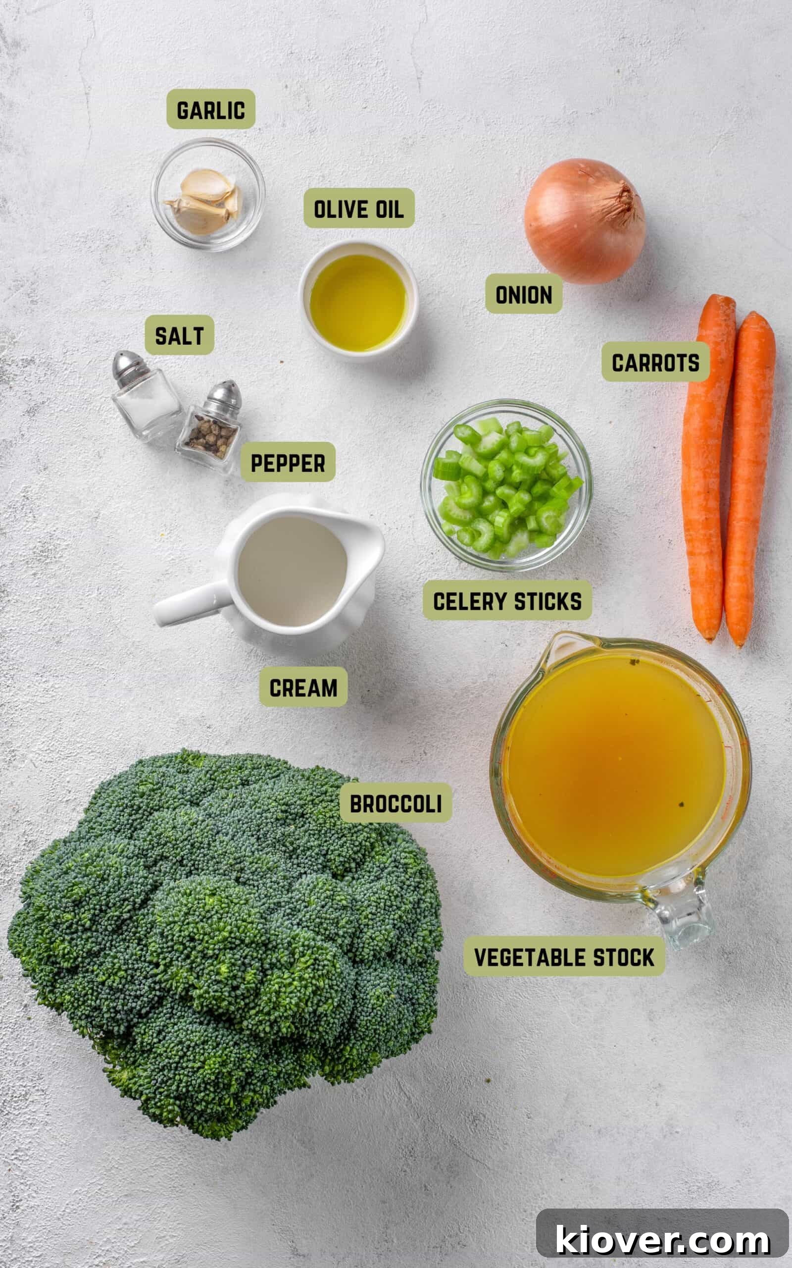 Fresh ingredients laid out on a wooden board, including broccoli, carrots, celery, onion, and garlic, ready for making soup.