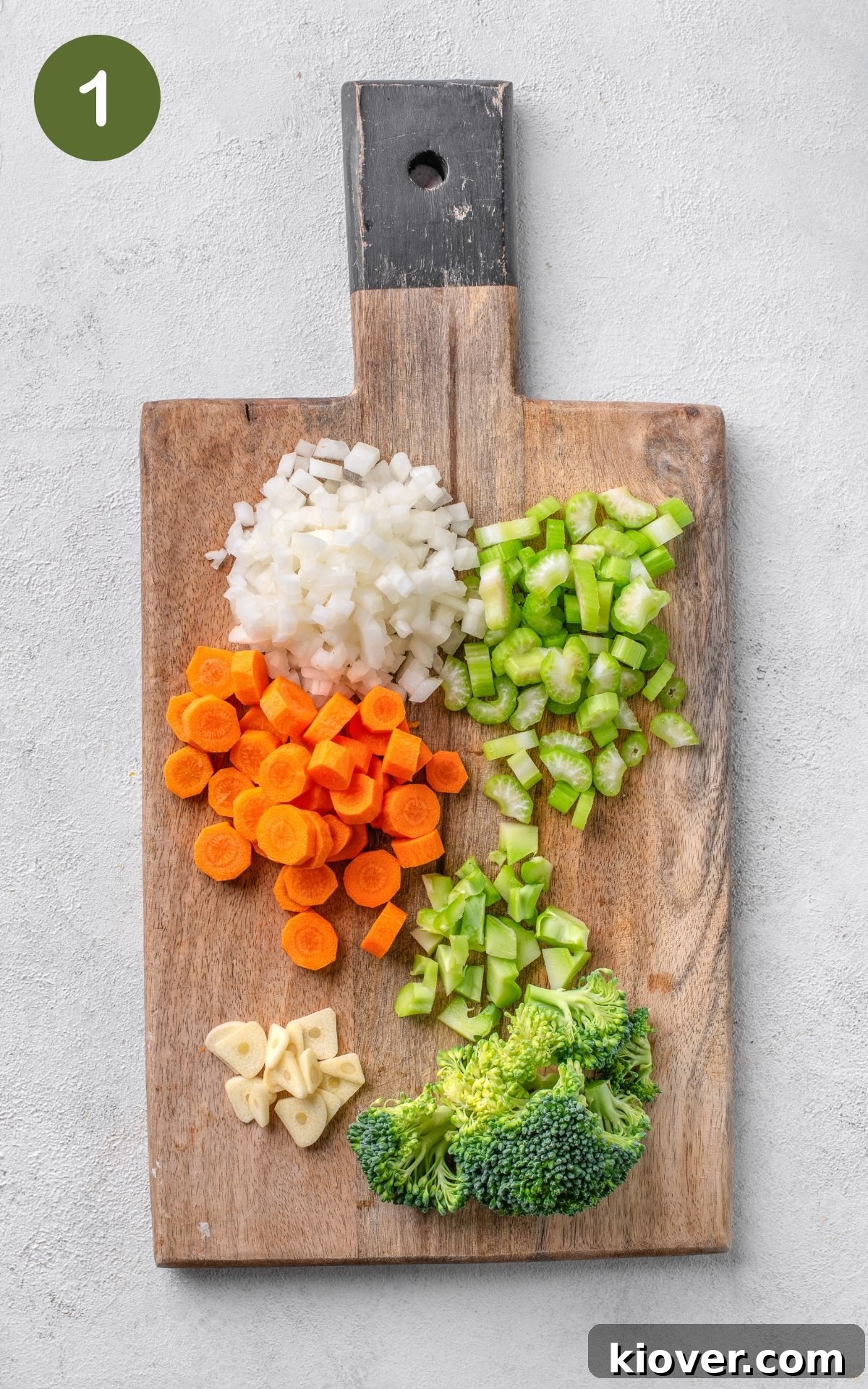 Colorful vegetables, including broccoli, carrots, onions, and celery, arranged on a wooden cutting board, ready for preparation.