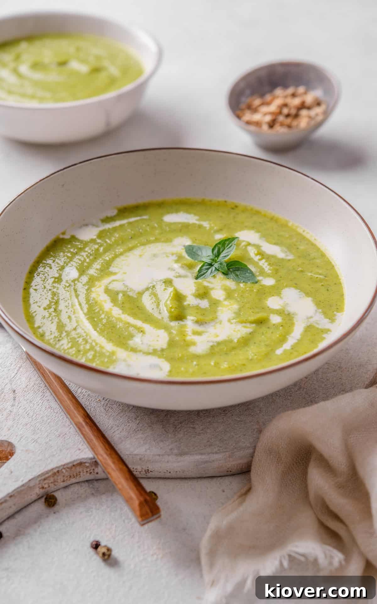 A bowl of creamy green soup, with broccoli florets and celery stalks as garnish.