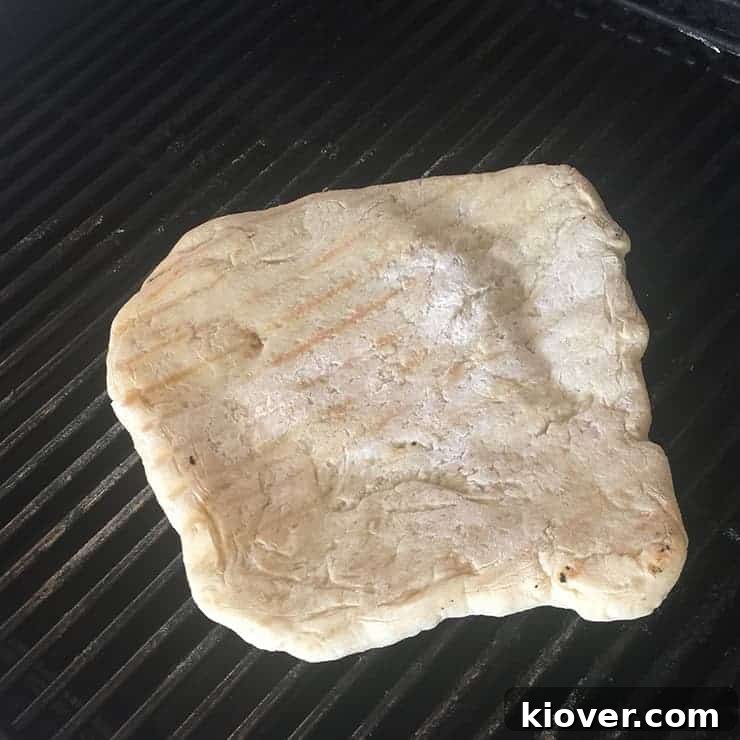 Grilling Pizza Dough First flip of the pizza dough on the grill, showing developing char marks.