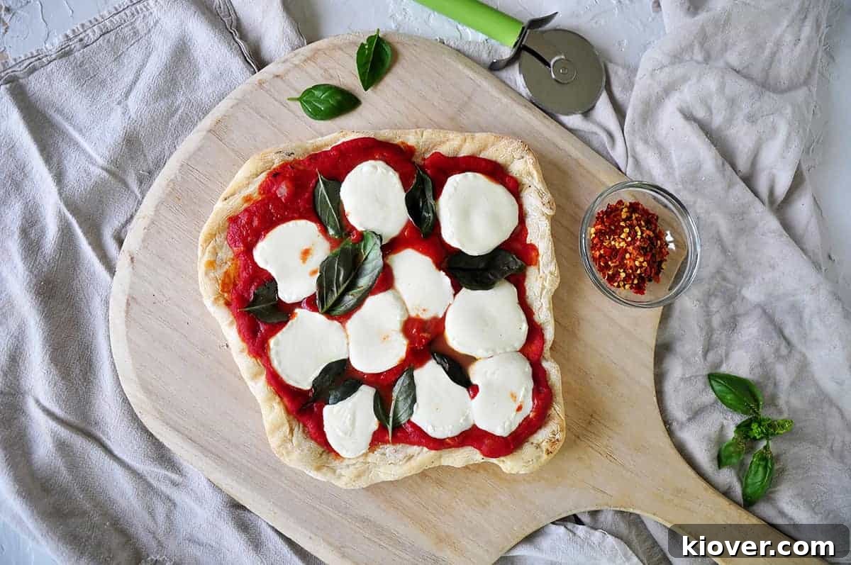 Weber Pizza Full weber pizza on a wood pizza peel with fresh basil and red pepper flakes to the side. A delicious grilled pizza ready to be served.