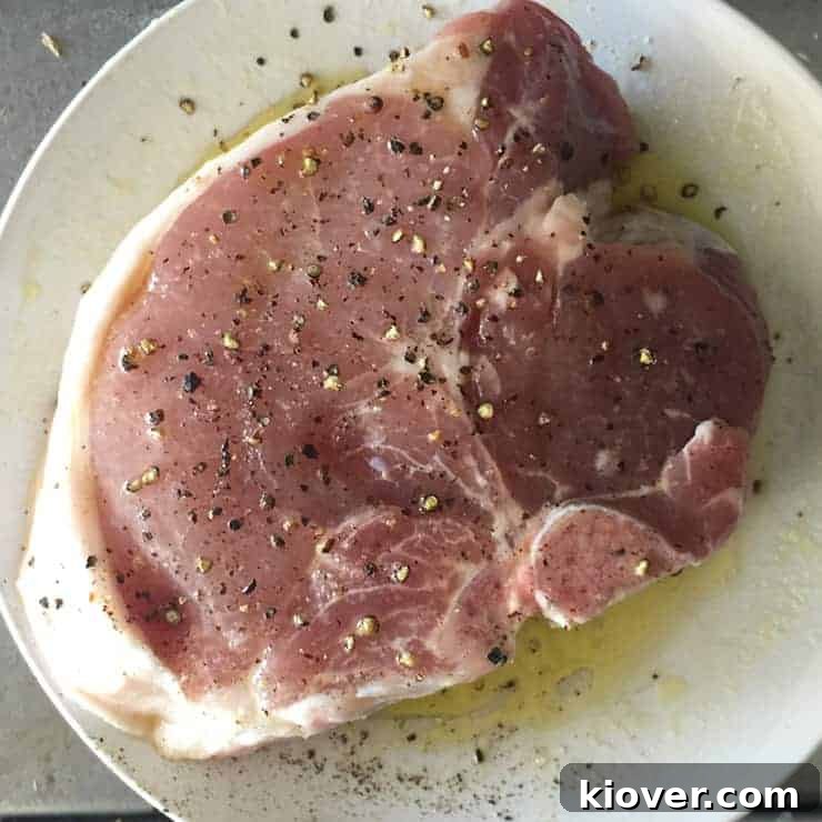 Raw pork chop coated in olive oil, salt, and pepper, ready for the grill.