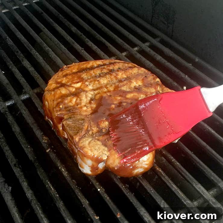 A pork chop grilling over indirect heat, being brushed with homemade BBQ sauce.