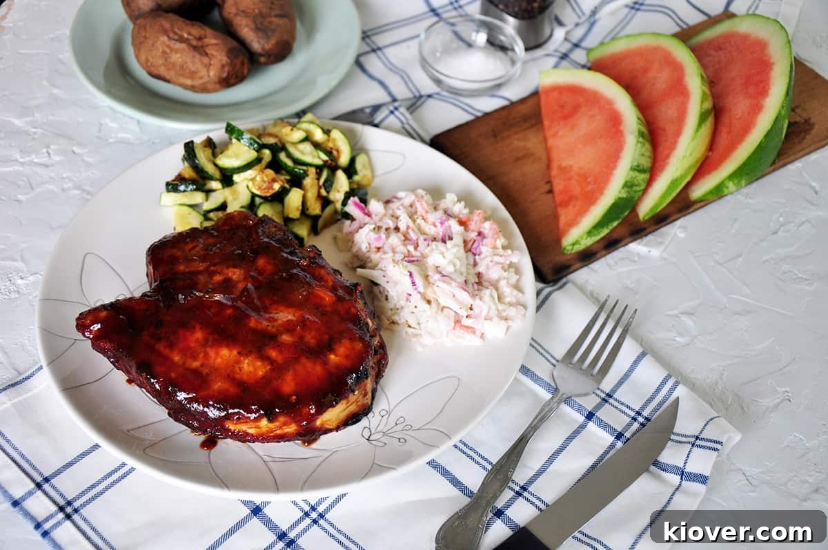 Completed pork chops served on a plate with grilled zucchini, creamy coleslaw, and refreshing sliced watermelon in the background.