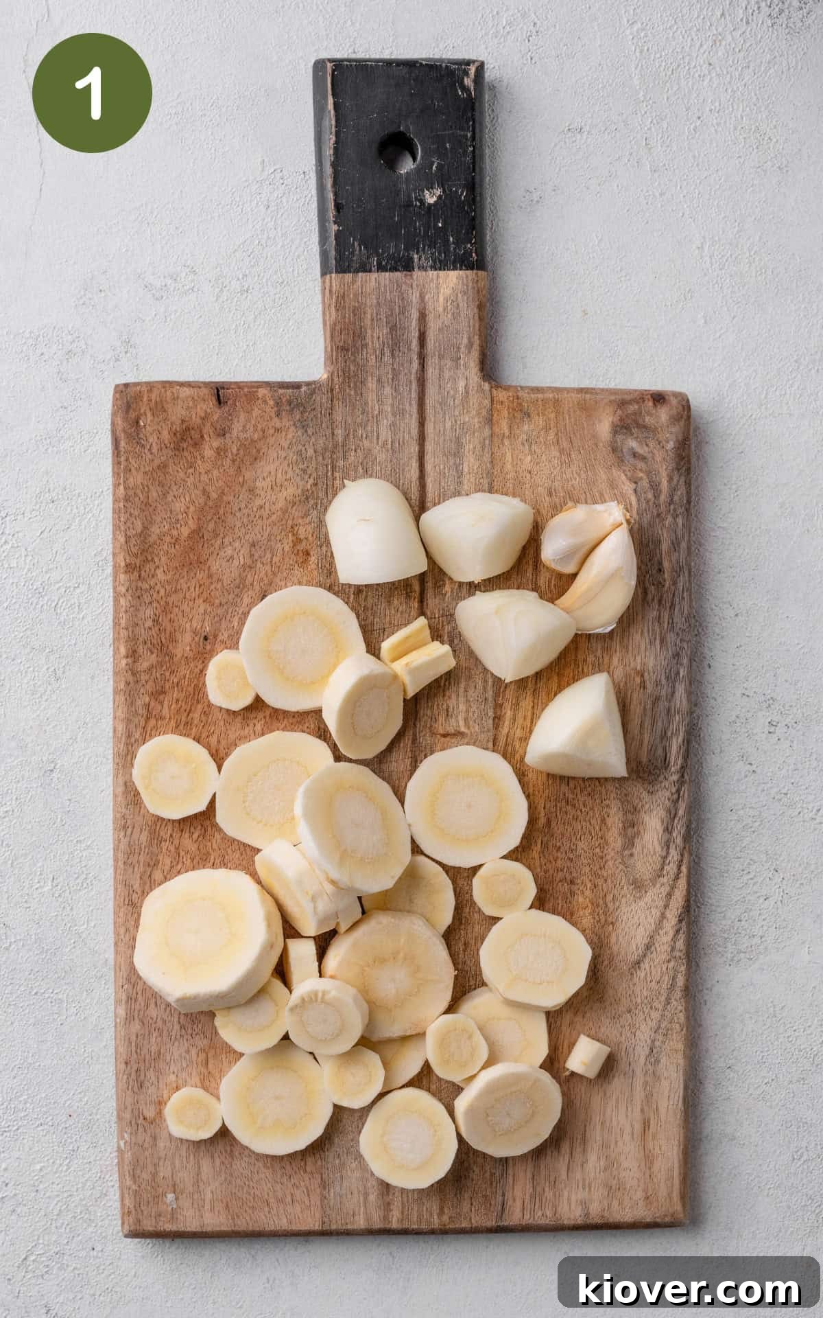 Peeled and chopped parsnips and onions, with whole garlic cloves, on a wooden cutting board.