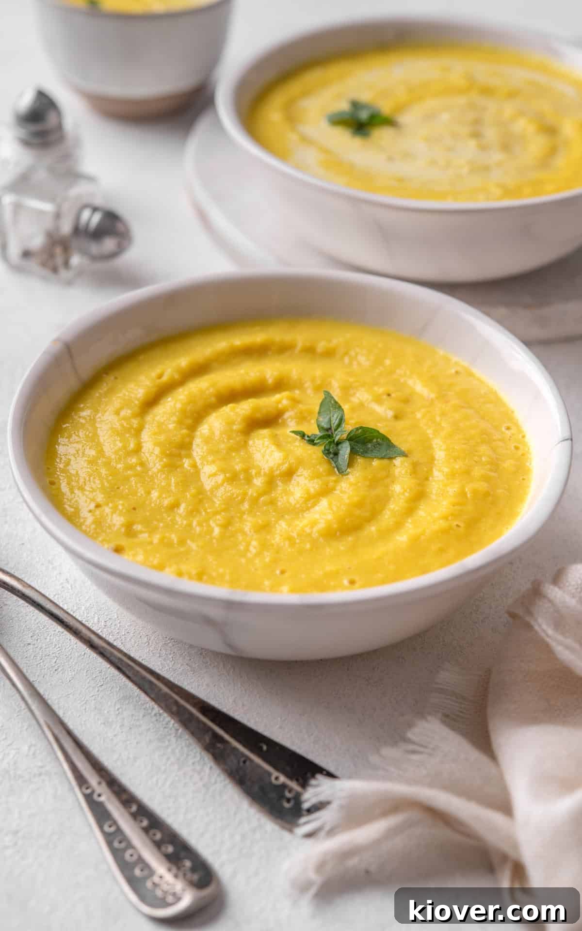 Simple curried parsnip soup in a bowl, garnished with a swirl of cream and fresh herbs.