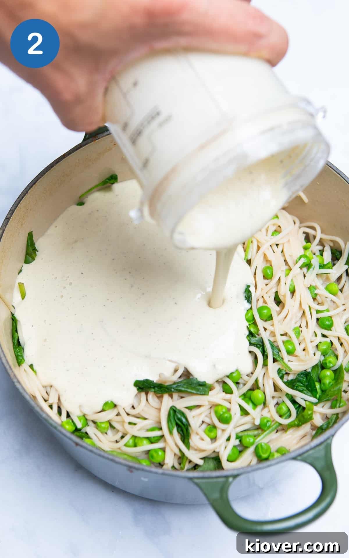 Creamy carbonara sauce being added to drained spaghetti and wilted spinach in a large saucepan.