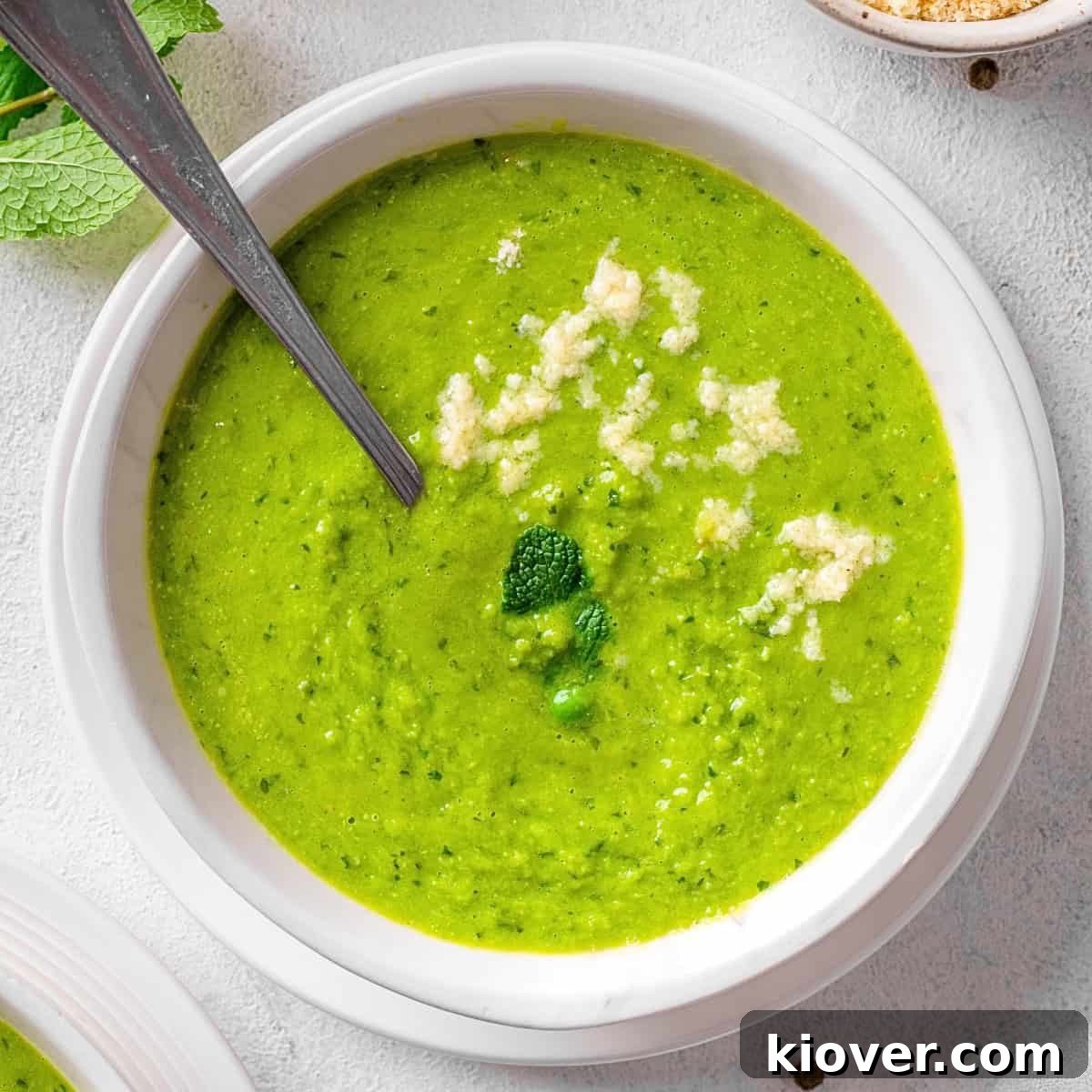 Silky Minted Pea Soup 2 A bowl of vibrant green pea and mint soup, garnished with fresh mint leaves and a drizzle of cream.