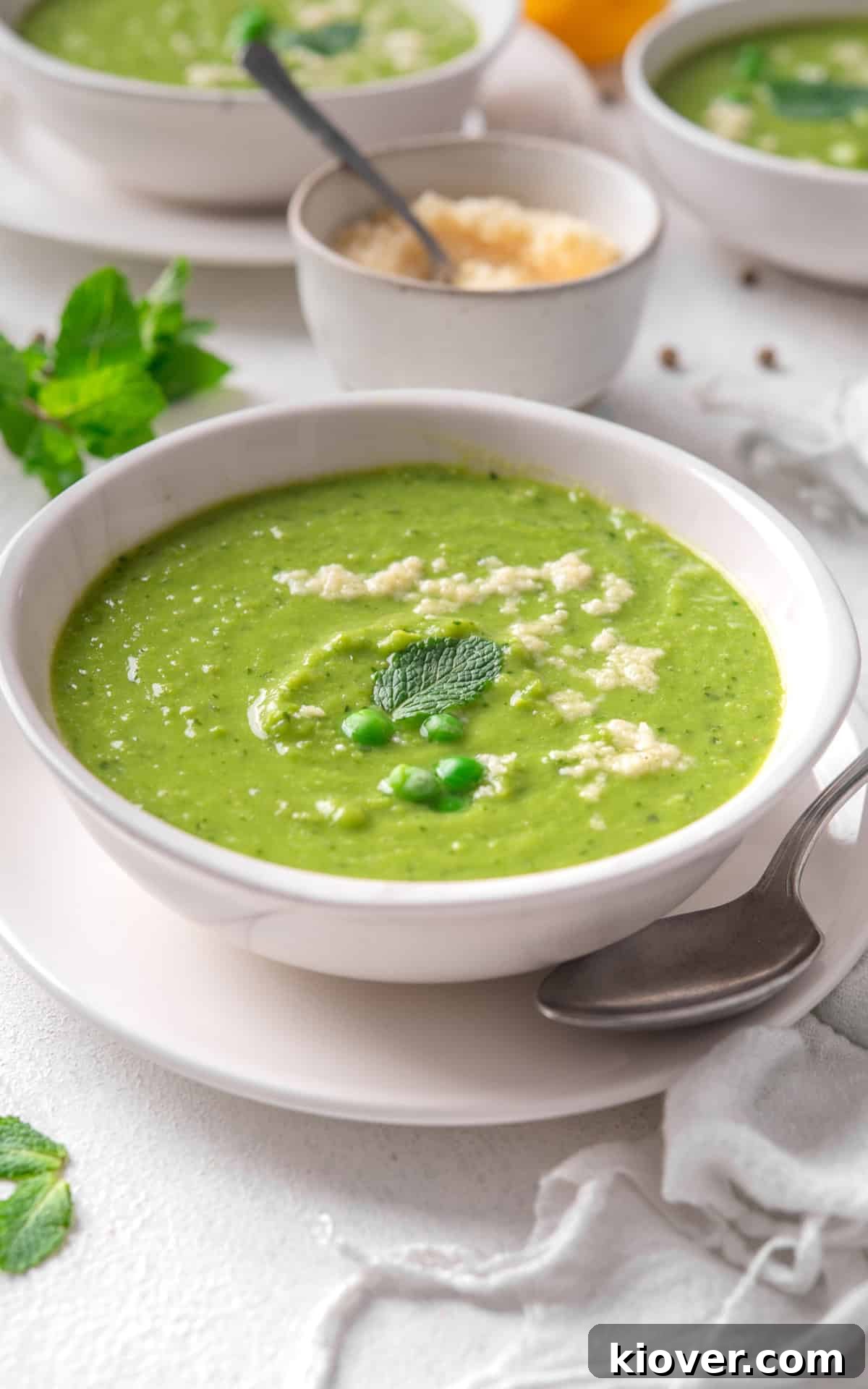 Silky Minted Pea Soup 9 A bowl of vibrant green pea and mint soup, garnished with fresh mint, a swirl of cream, and grated parmesan cheese.