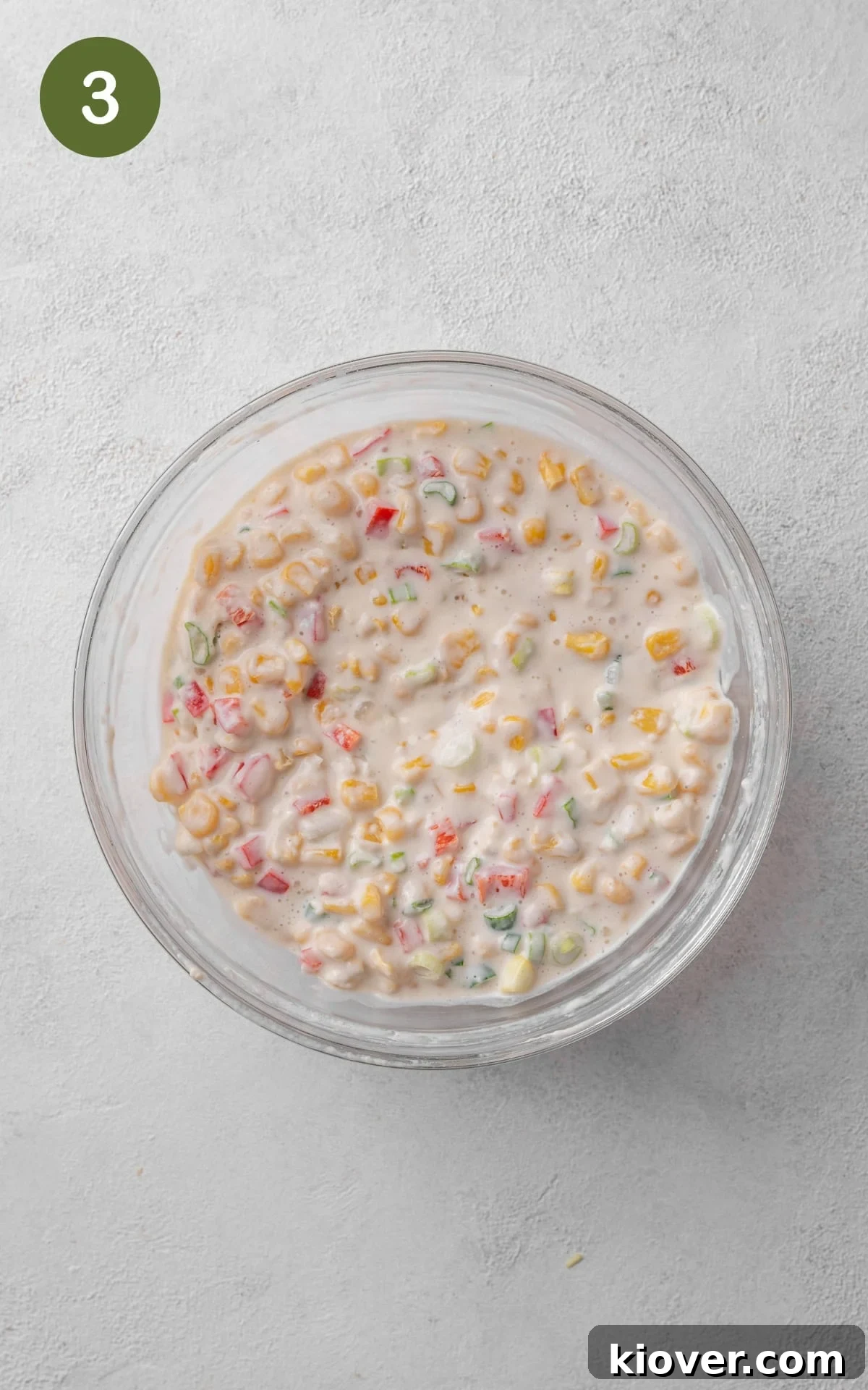 A close-up of chopped vegetables and thawed corn being stirred into the prepared fritter batter.