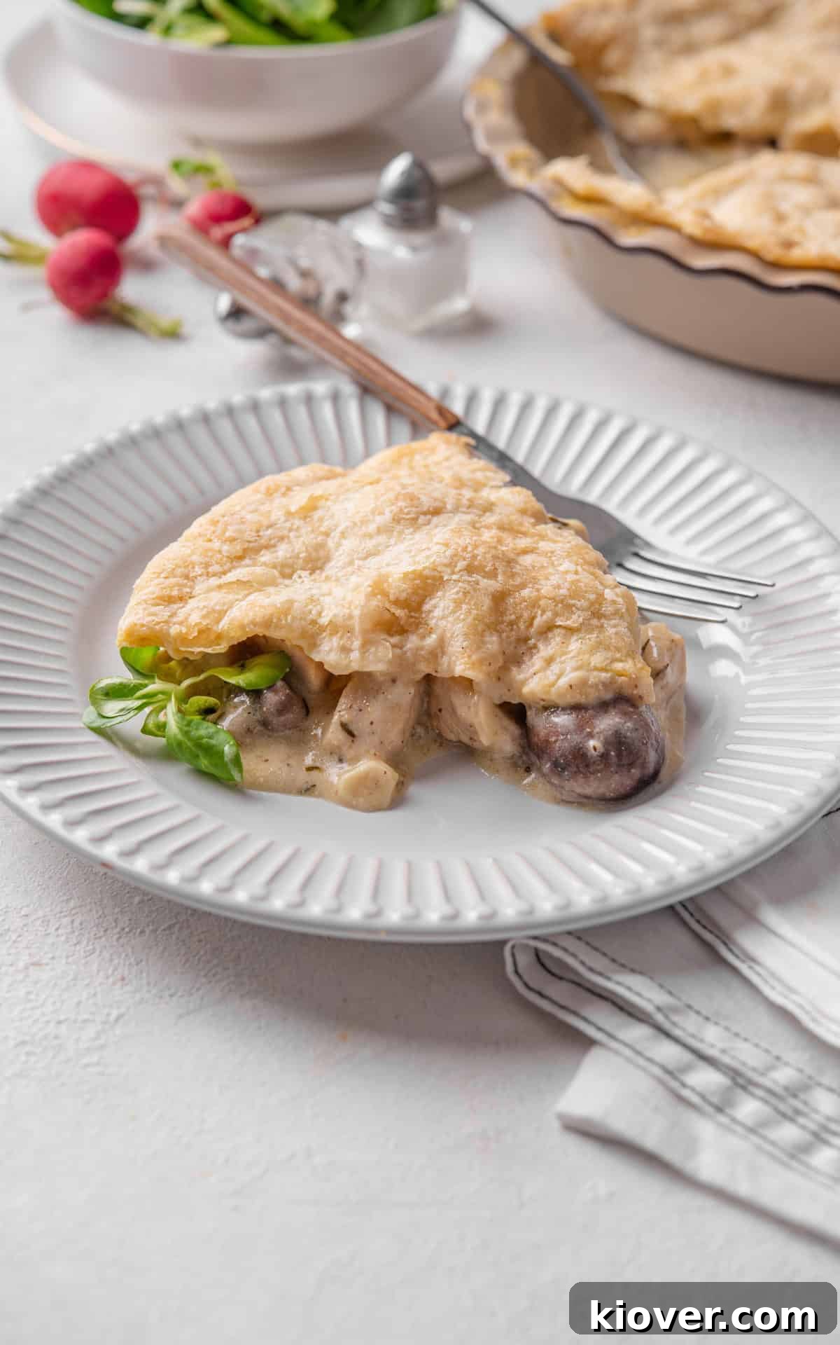 A generous slice of creamy chicken and mushroom pie on a white plate, showcasing the flaky crust and rich filling.