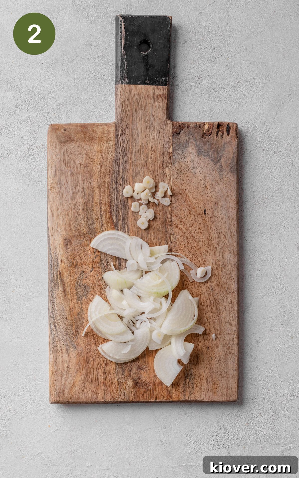 Sliced onions and minced garlic cloves on a cutting board.