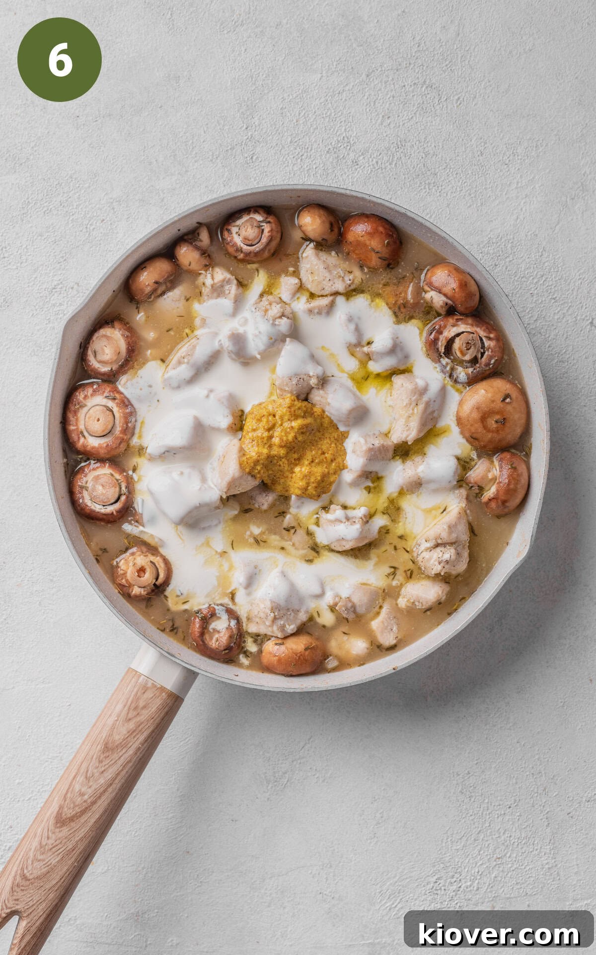 The creamy vegetable stock mixture with cream and mustard being combined with mushrooms and chicken in a skillet.