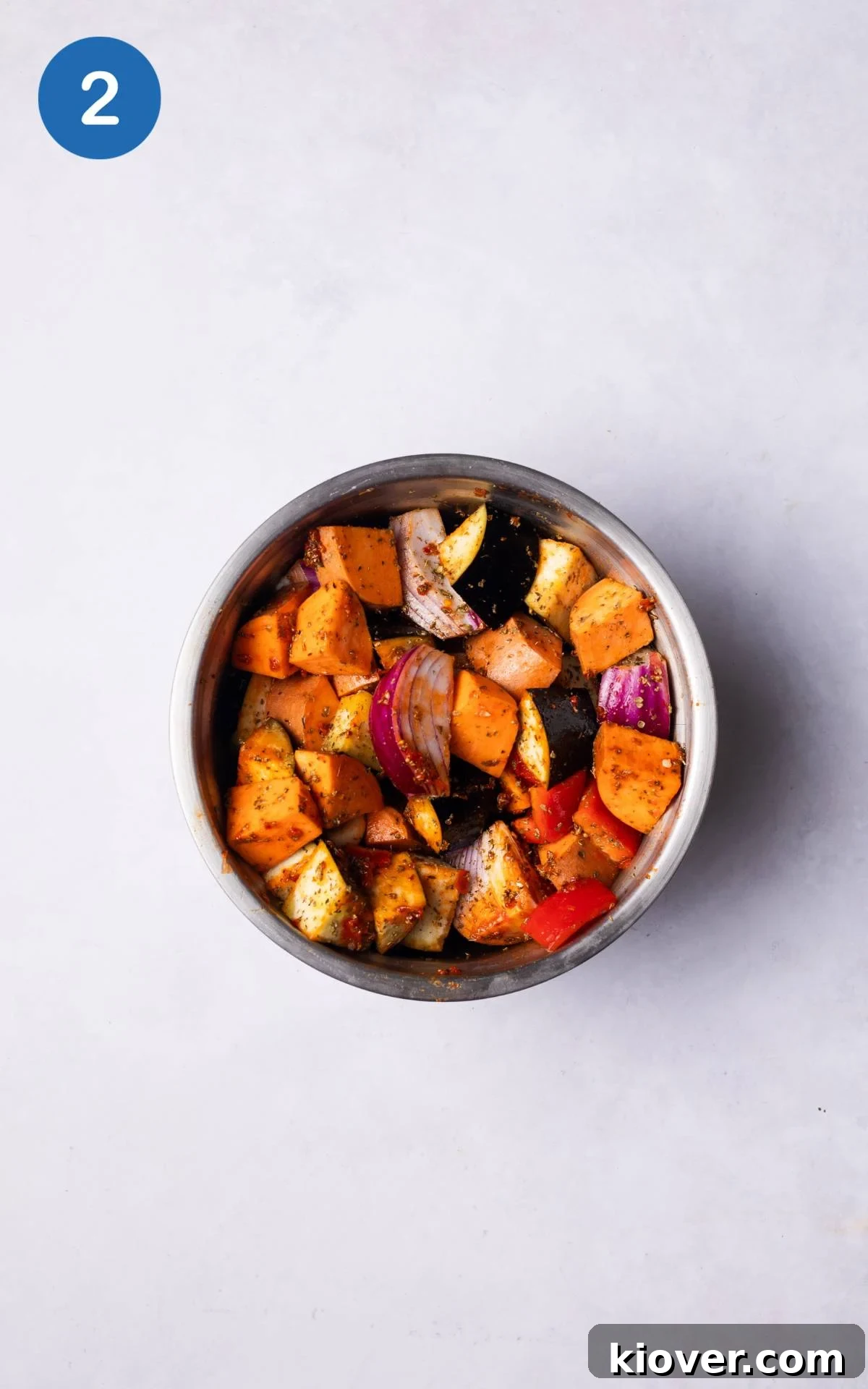 Sheet Pan Sausage Supper 5 Chopped vegetables generously coated with harissa paste, olive oil, and dried oregano in a large mixing bowl.