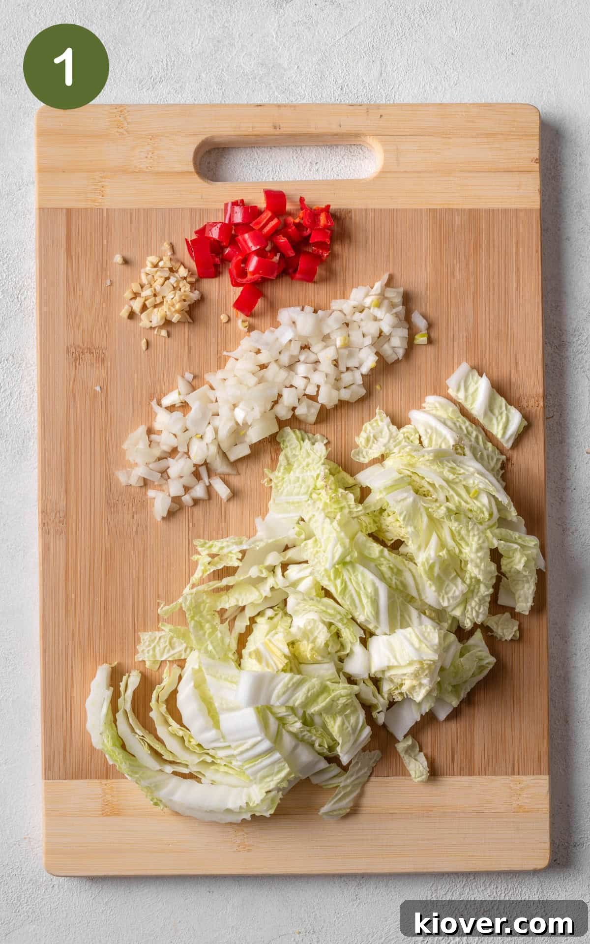 Freshly chopped onion, garlic, red chili, spring onion, and Chinese cabbage neatly arranged on a wooden cutting board, ready for stir-frying.