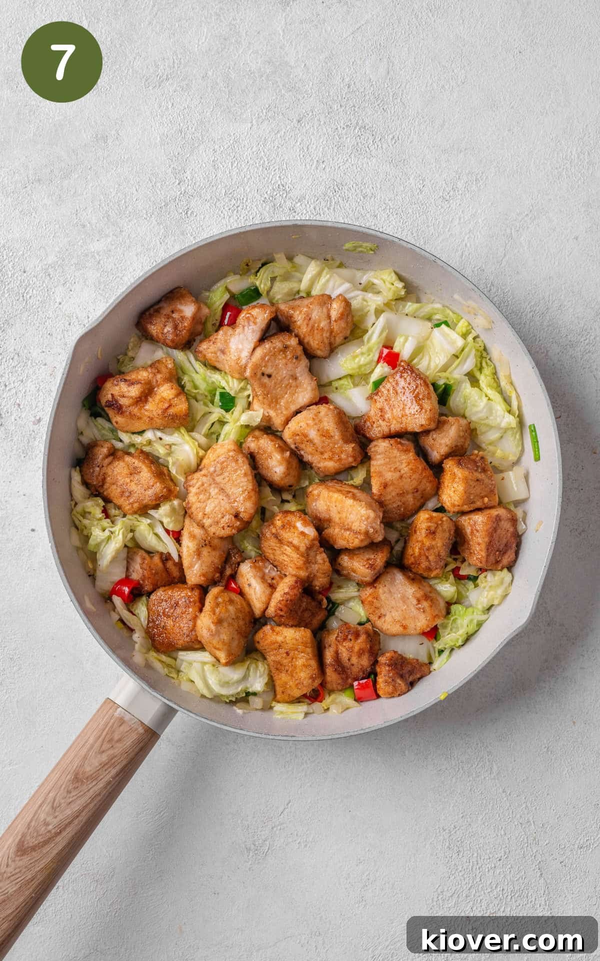 Crispy fried chicken pieces being tossed back into the skillet with sautéed vegetables, ensuring every component is perfectly combined.