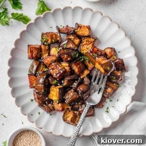 Roasted aubergine served on a plate, garnished with sesame seeds and parsley.