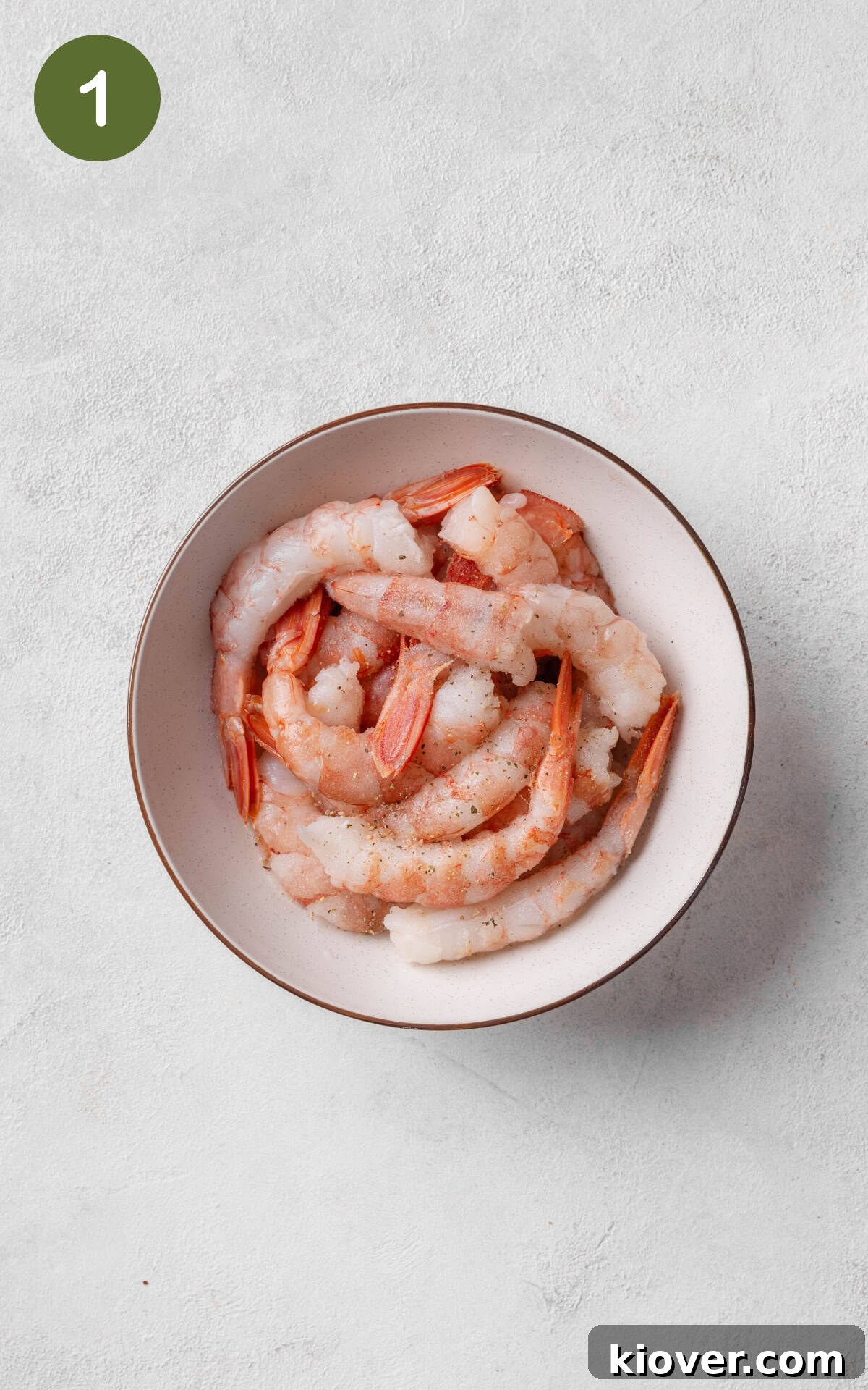 Prawns seasoned with salt and pepper in a mixing bowl, ready for cooking.