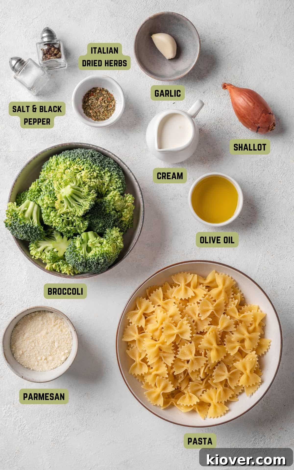 Arrangement of fresh ingredients for broccoli pasta: dry pasta, olive oil, shallot, garlic, a head of broccoli, parmesan cheese, cream, Italian dried herbs, and a lemon.
