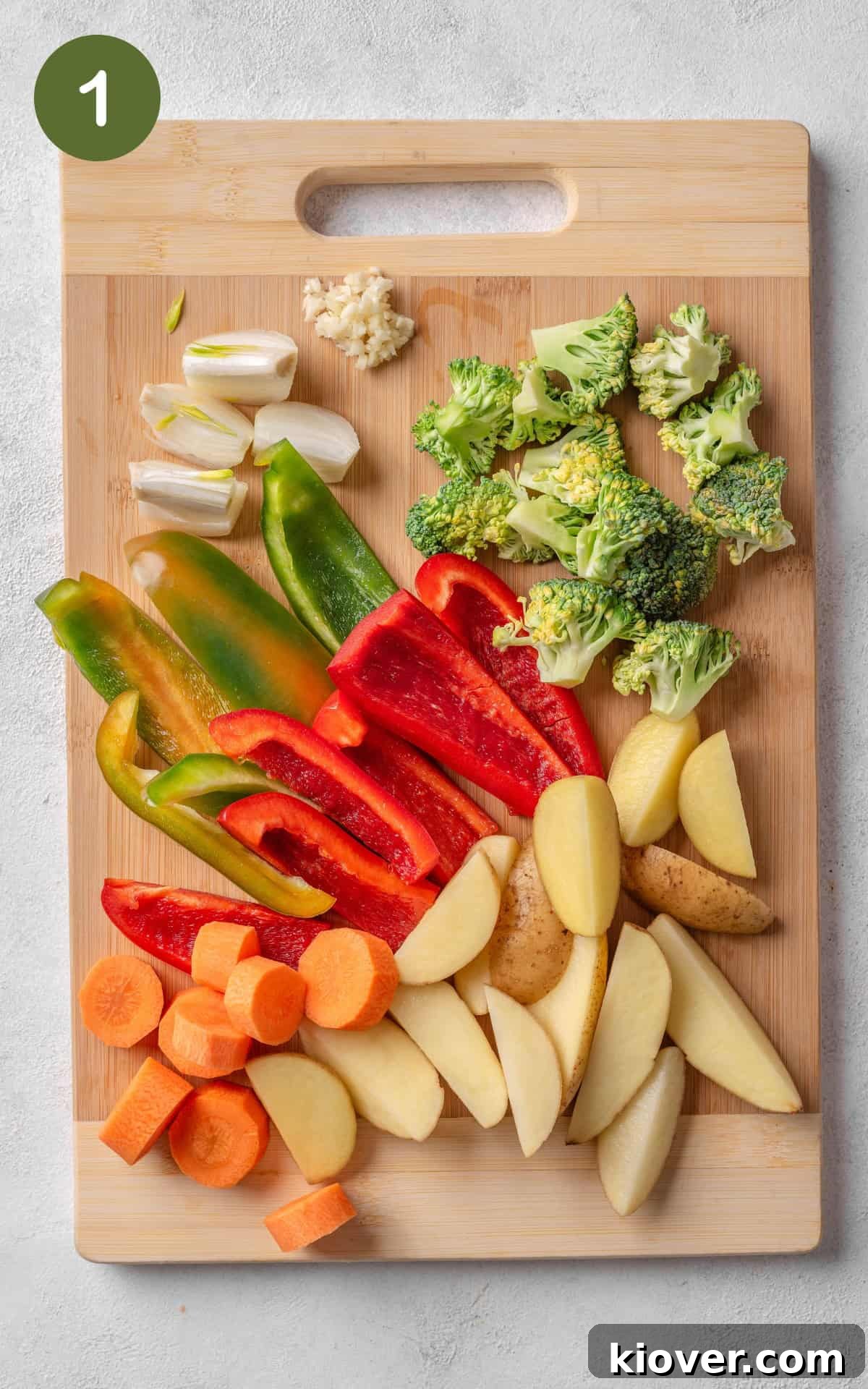 Various cut-up vegetables, including carrots, potatoes, onions, and bell peppers, arranged on a cutting board, ready for roasting.