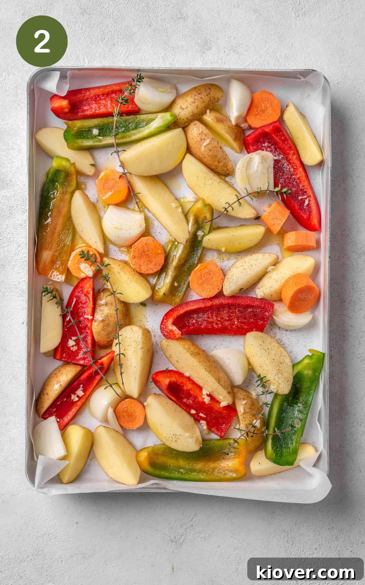 Assorted cut-up vegetables, including potatoes, carrots, onions, and bell peppers, spread evenly on a baking tray, drizzled with oil and seasoned.