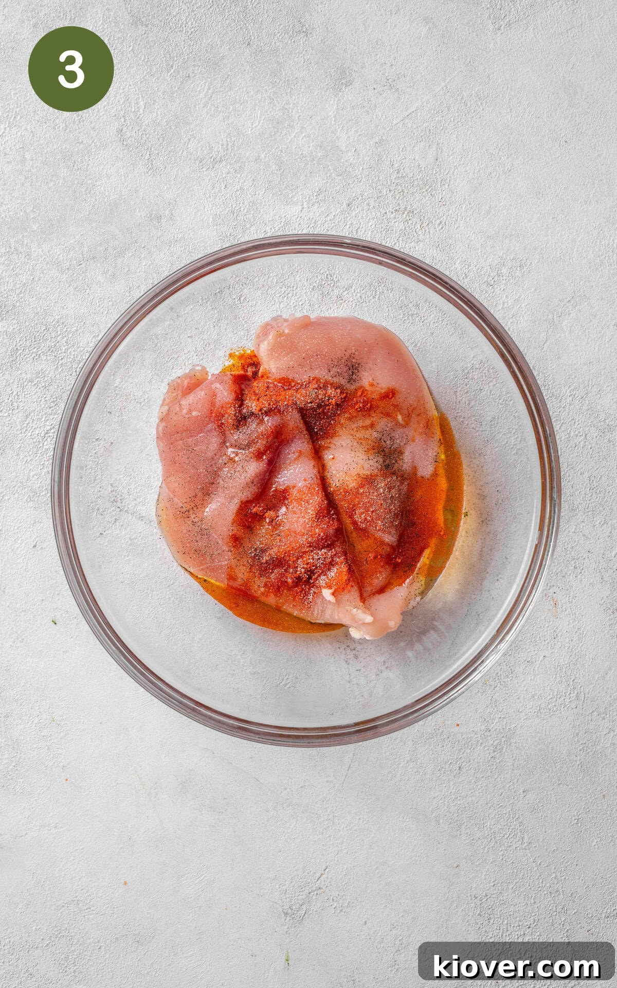 Raw chicken breasts seasoned with salt, pepper, and paprika, mixed with olive oil in a bowl, ready for cooking.