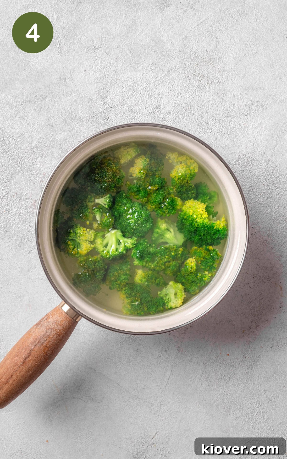 Fresh broccoli florets cooking in simmering water in a saucepan.