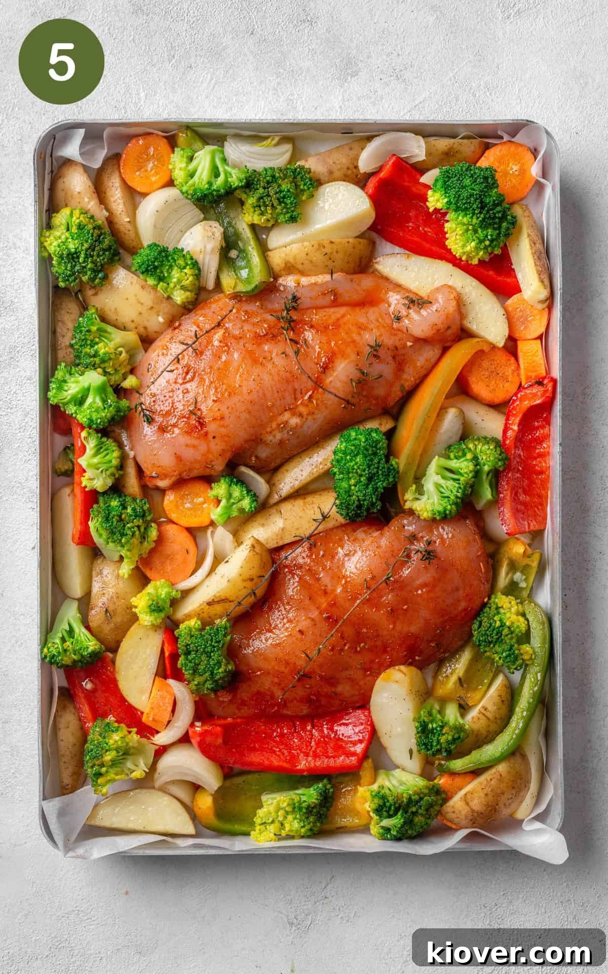 Seasoned chicken breasts and par-cooked vegetables, including blanched broccoli, arranged on a baking tray, ready for final roasting.