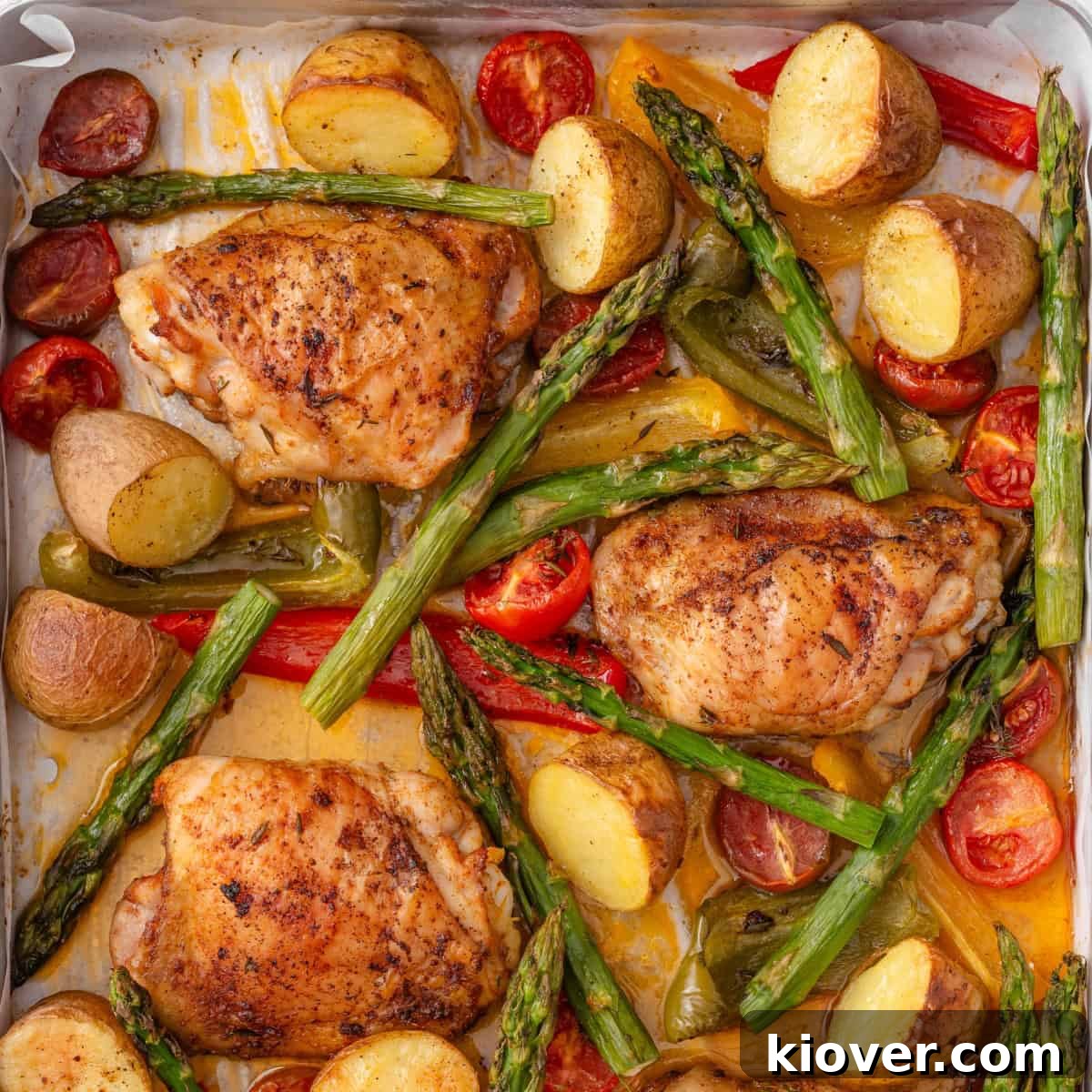 Roasted chicken thighs with vibrant vegetables arranged on a baking sheet, fresh out of the oven.