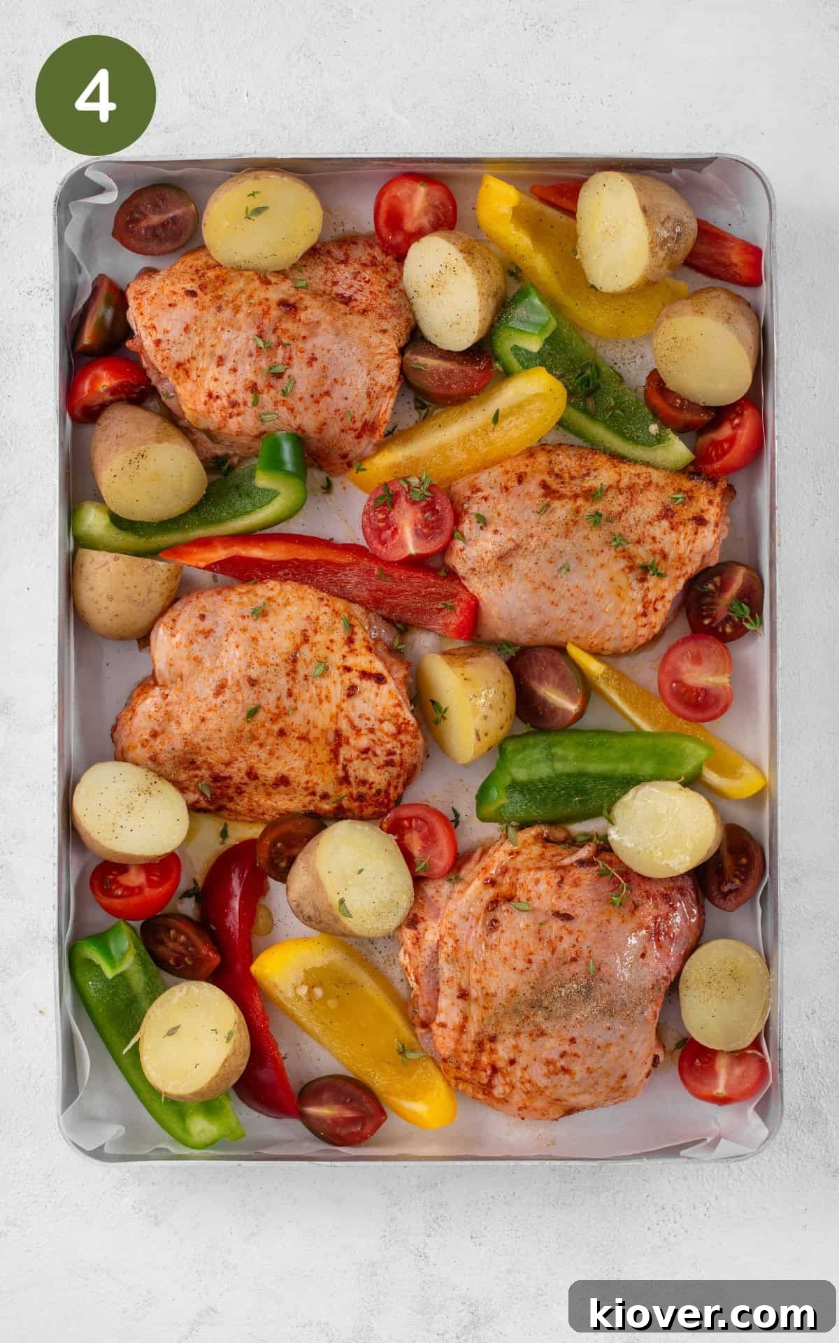Chicken thighs, potatoes, and bell peppers arranged on a baking tray, ready for roasting.