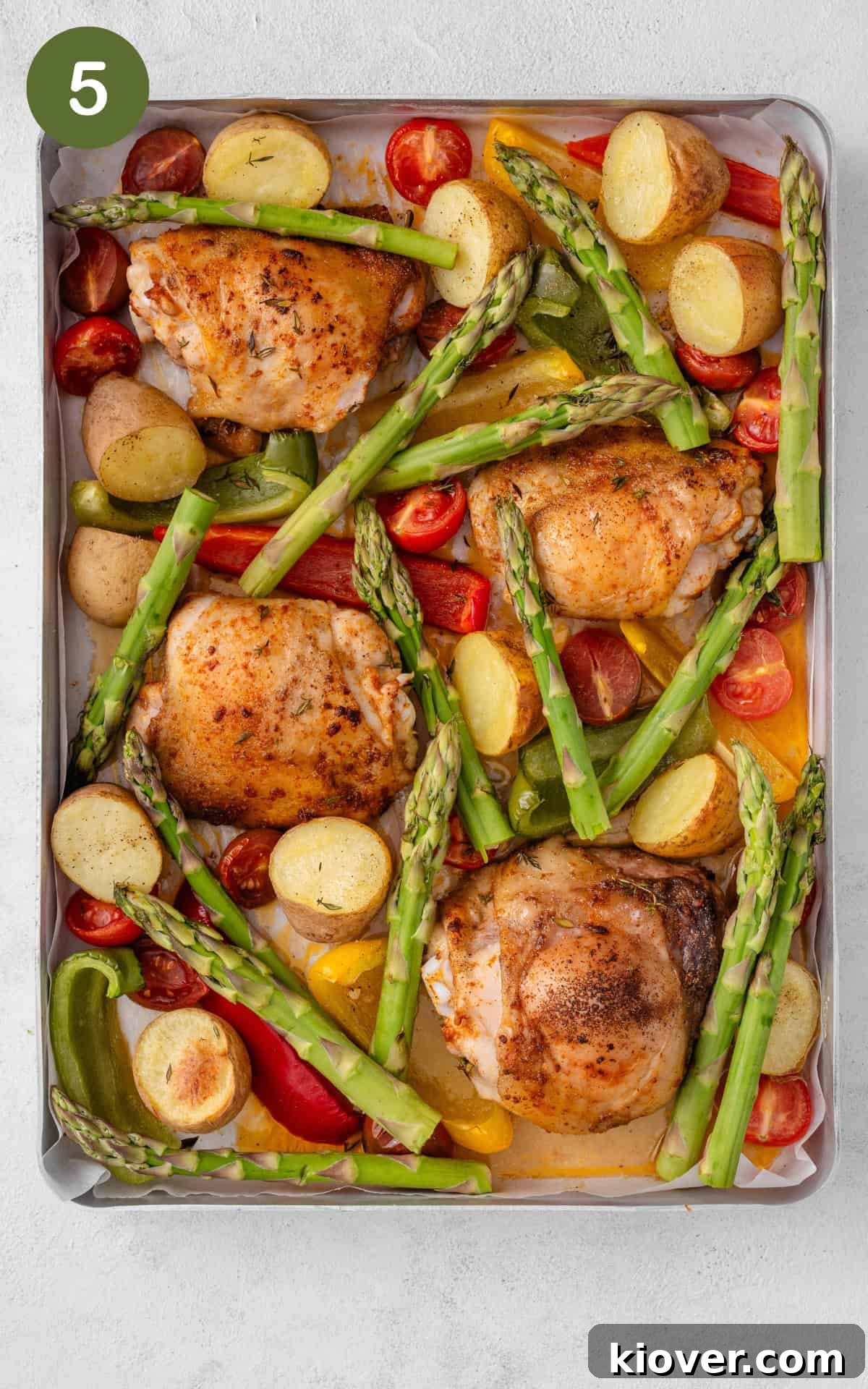 Chicken thighs, asparagus, and other vegetables on a baking tray, cooked to perfection.