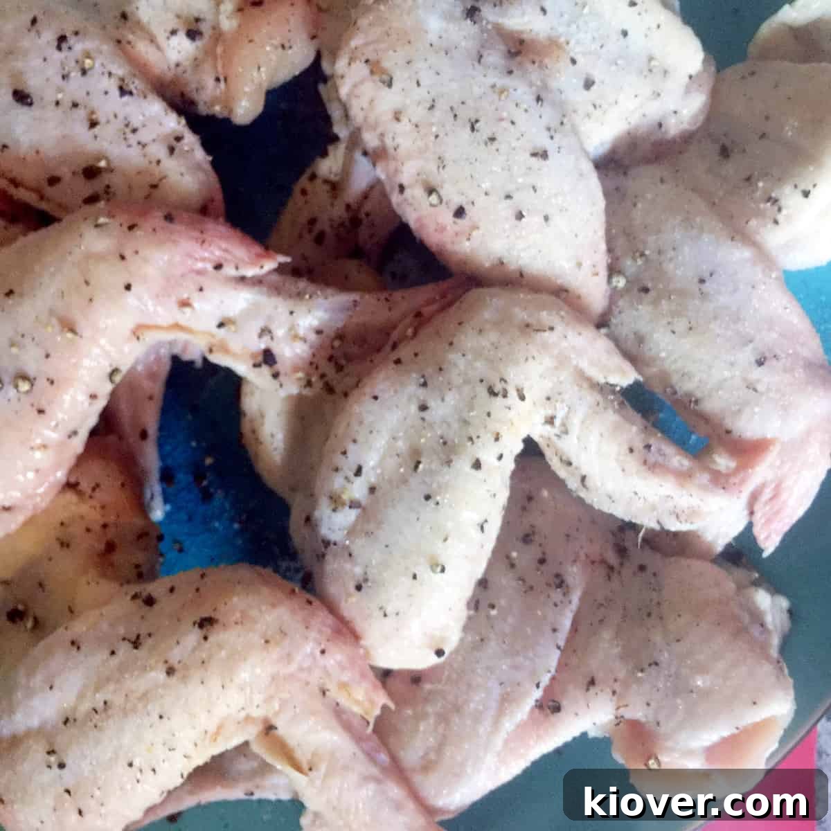 Chicken Wings Raw chicken wings, generously seasoned with salt and pepper, arranged on a surface, ready for grilling.