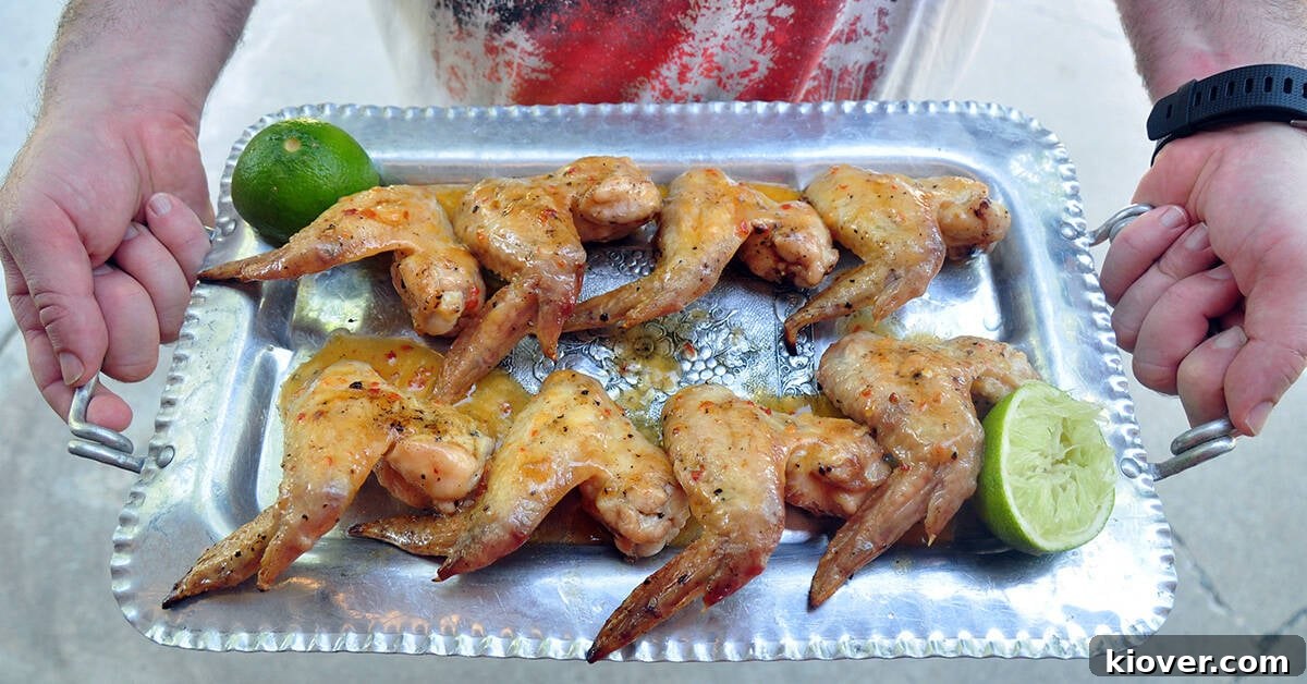 Tequila Lime Chicken Wings Eight full, beautifully grilled chicken wings artfully arranged on a silver platter, held up by two hands, showcasing their perfect golden-brown crispness.