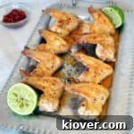 Eight Grilled Tequila Lime Chicken Wings on a silver platter getting ready to be served. There are two spent limes and a dish of samal oelek in the background.