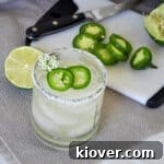 Watermelon Spicy Margarita on a white mat wihth jalepeno slices and a lime half in the background