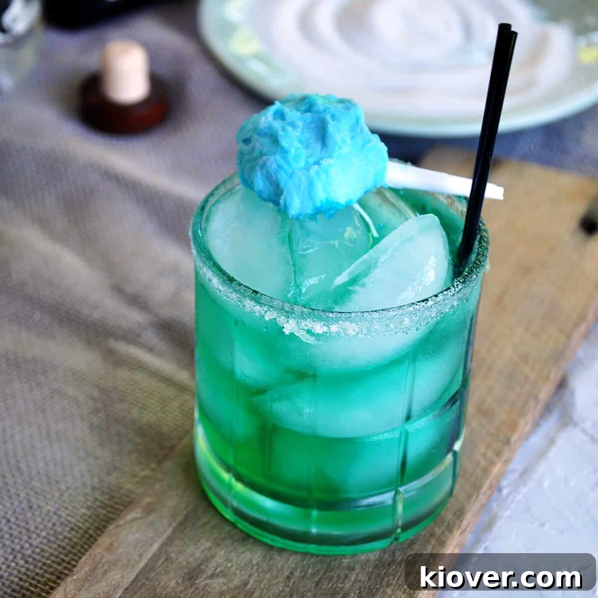 Cotton Candy Margarita on a wood plank with a small cotton candy garnish and two black straws.