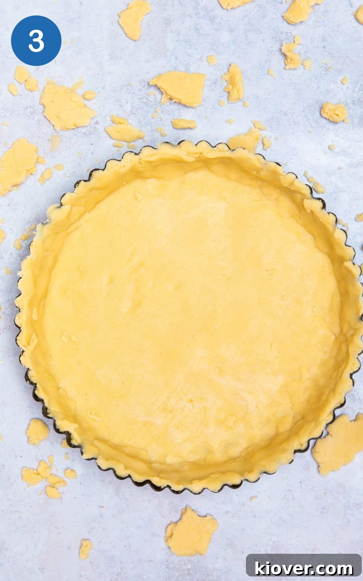 The rolled-out pastry neatly placed into a fluted tart tin, ready for filling, on a grey marble surface.