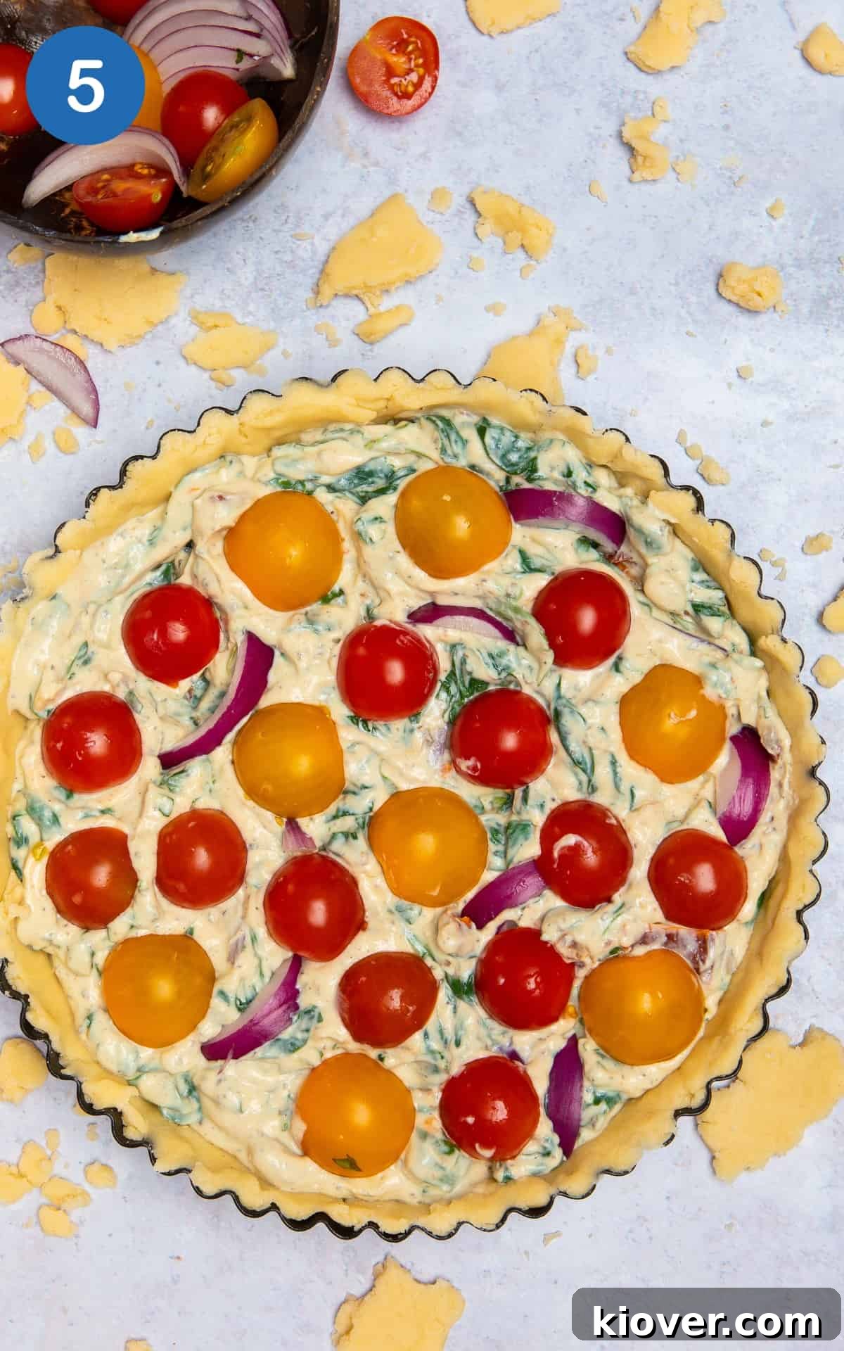 The unbaked vegan quiche, beautifully topped with fresh sliced tomatoes, ready for the oven, on a grey marble background.