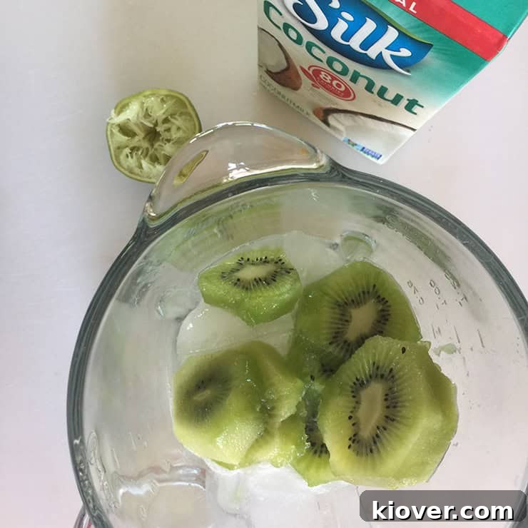 Freshly sliced kiwi pieces being added to a blender, with a carton of Silk Coconut milk visible in the background, ready to be transformed into a refreshing frozen margarita.