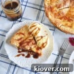 Overhead view of one slice of apple pie with two scoops of vanilla ice cream and caramel sauce in the background.