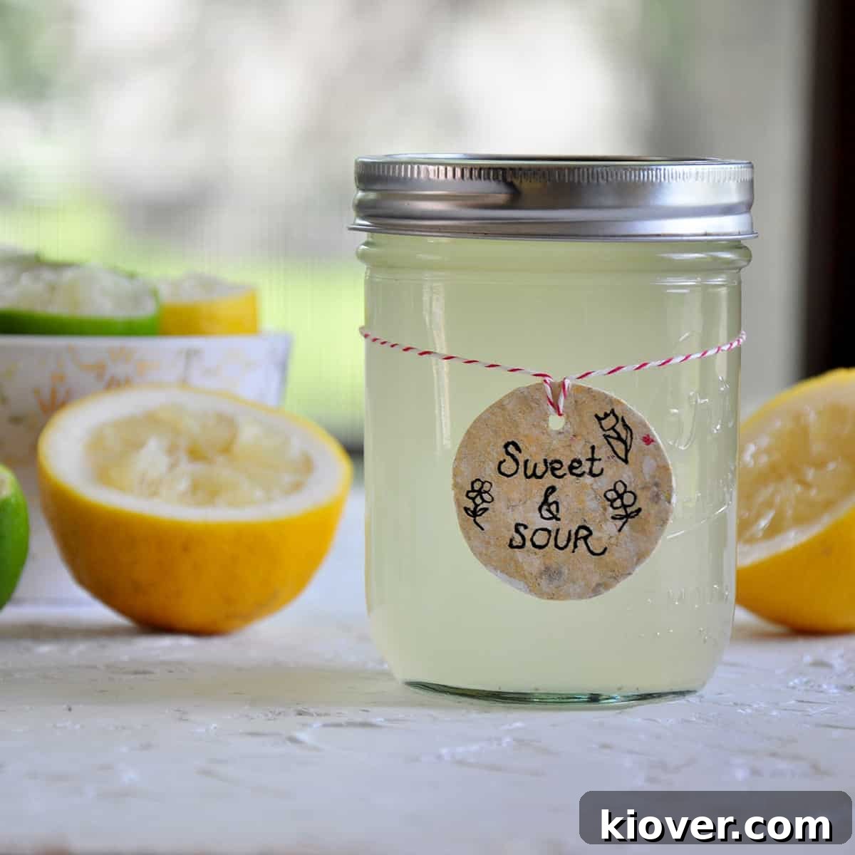 Homemade Sweet and Sour Mix for Cocktails A glass jar filled with vibrant homemade sweet and sour mix, surrounded by fresh lemons and limes, set on a rustic wooden surface, highlighting natural ingredients and freshness.