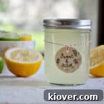 A glass jar of homemade sweet and sour mix with lemons and limes in the background, ready for cocktail making.