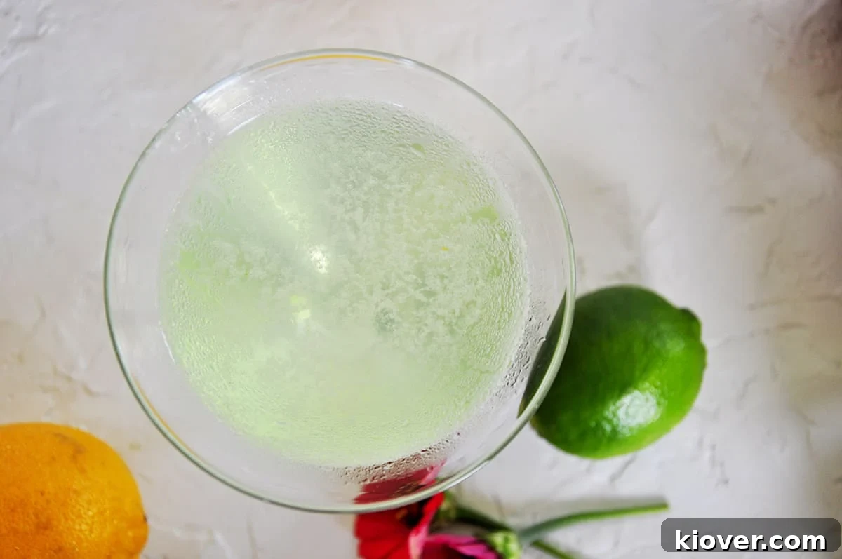 An overhead shot of a vibrant green Appletini cocktail in a martini glass, with an apple slice garnish.