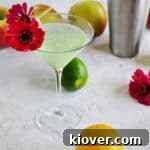 Appletini with lemons, limes, apples and flowers in the background.