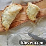 One whole Hand Pie and on that is cut in half. It is sitting on a rustic wooden cutting board and on top of some parchment paper