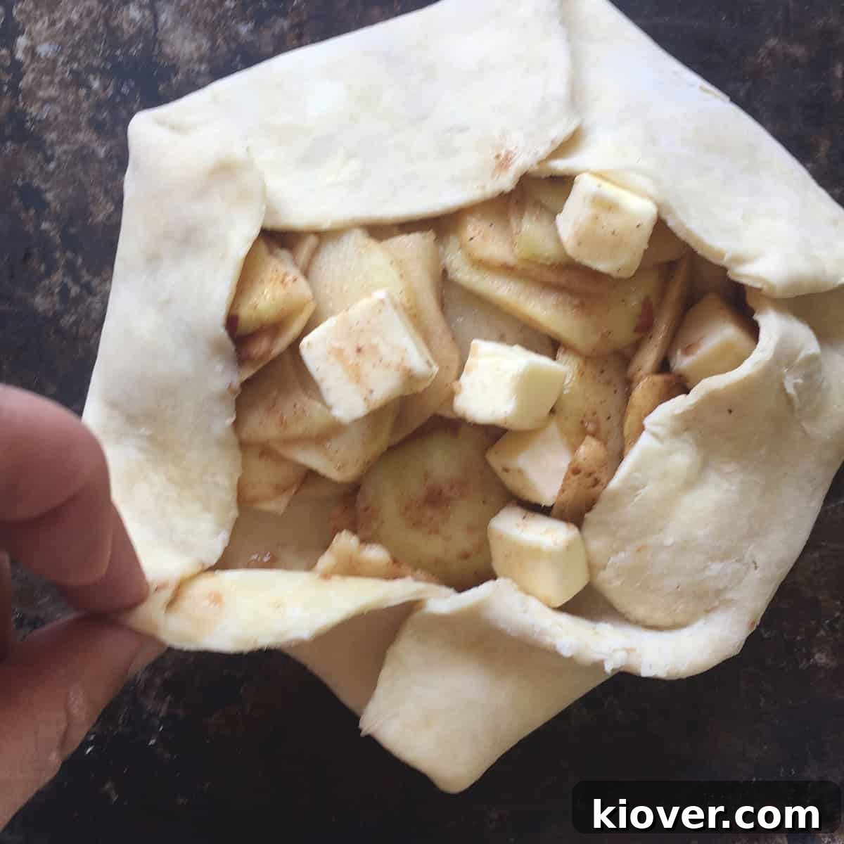 Folding a pie crust around some apple pie filling and butter, illustrating the assembly process of the crostata.