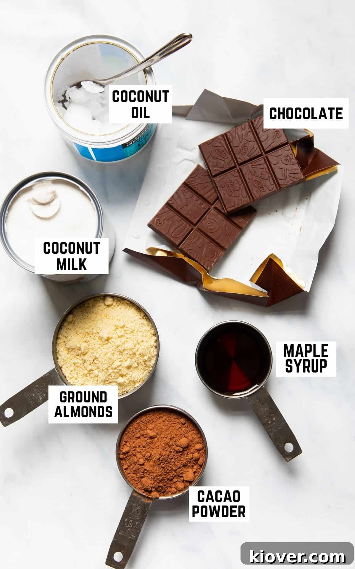 A beautifully arranged flatlay of the six key ingredients needed for the vegan chocolate tart: solid blocks of dark chocolate, a can of full-fat coconut milk, a bottle of maple syrup, a bowl of ground almonds, and a bag of cacao powder.