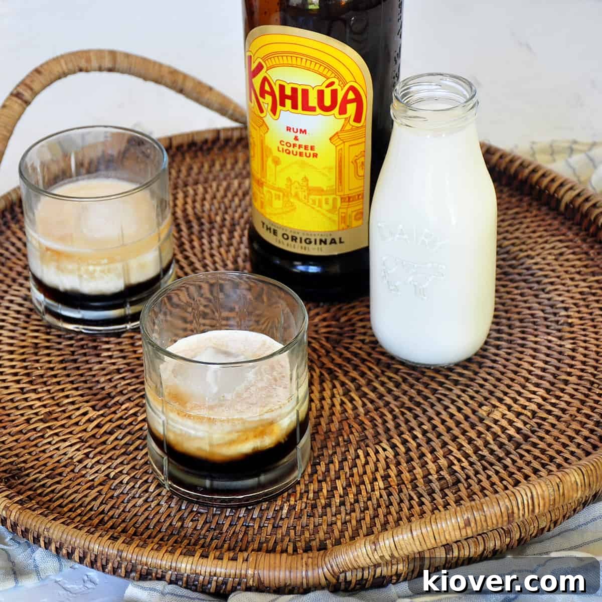 Two Classic White Russian cocktails, perfectly chilled and garnished, on a elegant serving platter, accompanied by a glass of fresh milk and a classic bottle of Kahlua. The scene evokes a sense of comfort and sophisticated indulgence.